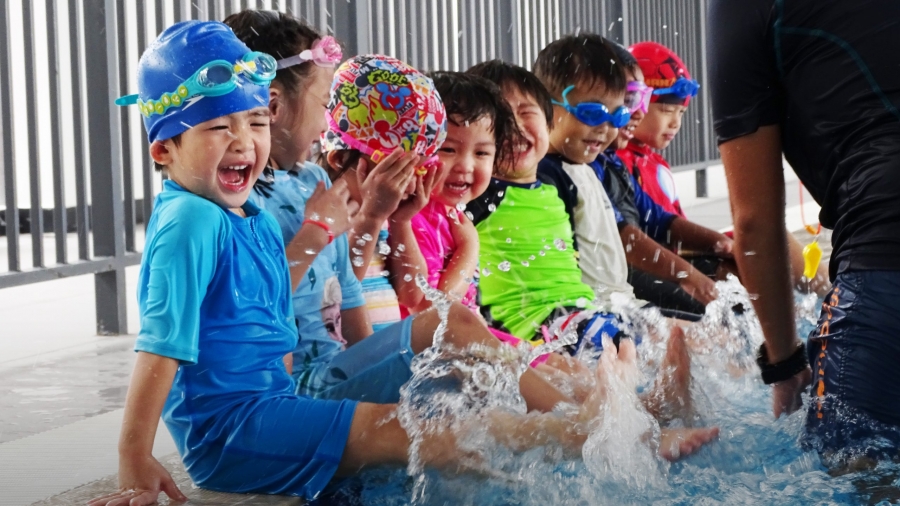 A group of children are playing and interacting with a teacher in the pool at Kingsley International School.